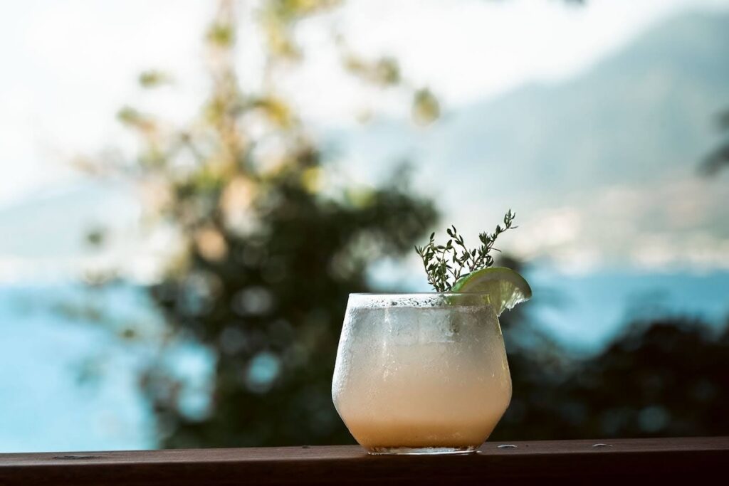 A floral pink cocktail sitting on the railing of the patio overlooking Tibay Beach and the mountains at Zing Zing, Secret Bay Dominica